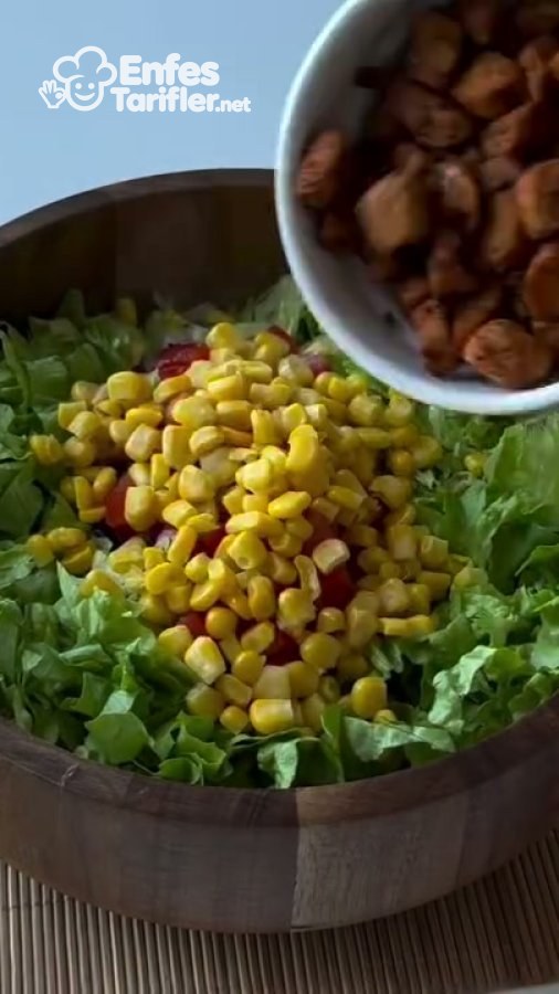 Marul ve mısır bulunan salata kasesine pişmiş tavuk parçalarının eklenmesi