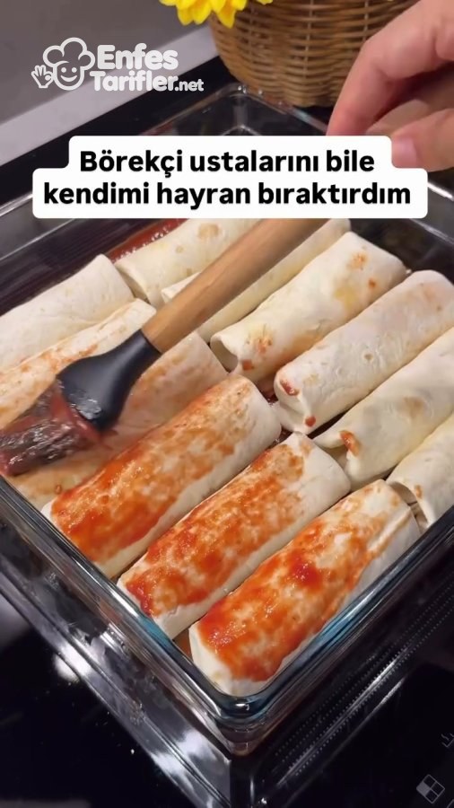 Fırın kabına dizilen lavaş böreklerinin üzerine domates sosu sürülmesi