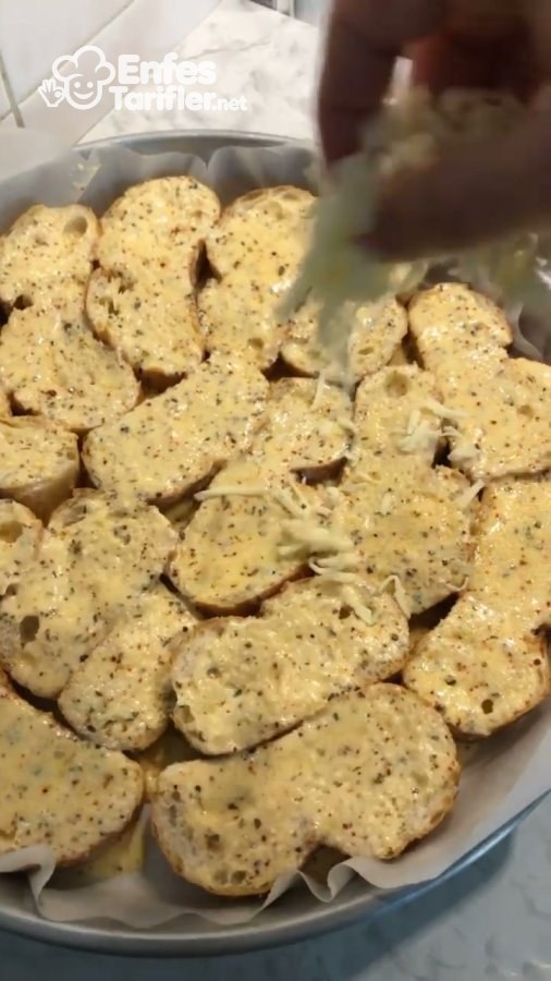 Tepsiye dizilen soslu ekmek dilimlerinin üzerine rendelenmiş peynir serpilmesi