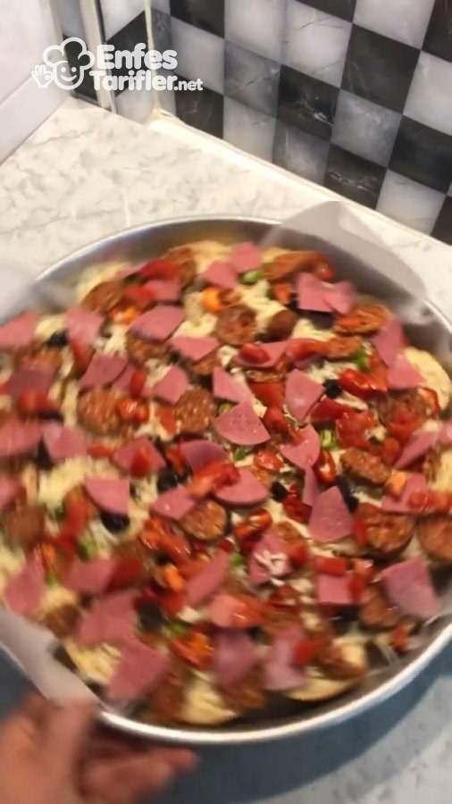 Ekmek dilimlerinin sucuk, salam, biber ve zeytinle kaplandığı pizza tepsisi