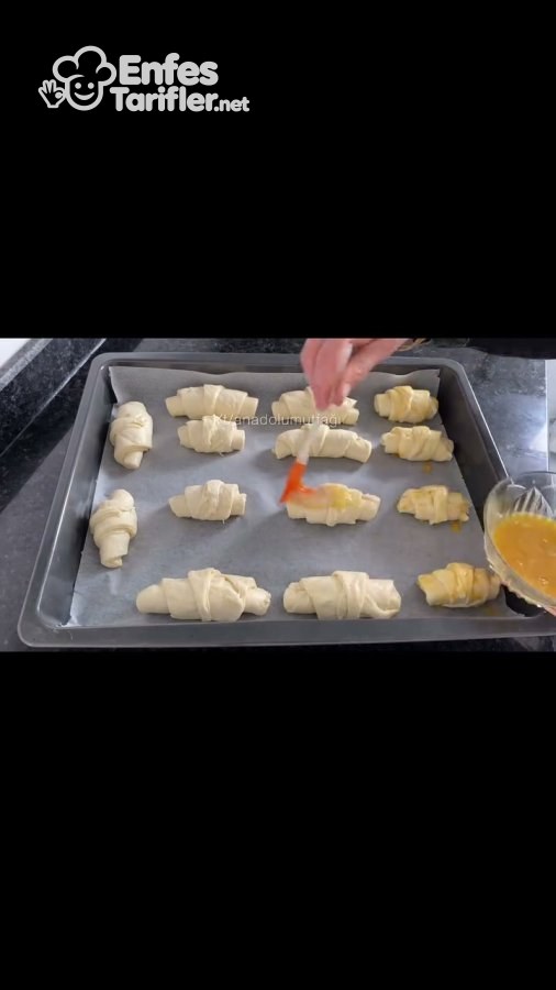 Tepsideki kruvasan poğaçaların üzerine fırçayla yumurta sarısı sürülmesi